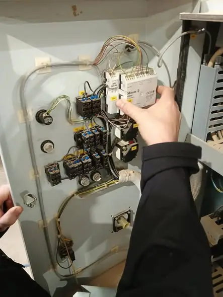 Hands testing wiring inside a control panel